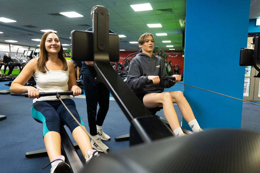Photo of two people using rowing machines in a gym.