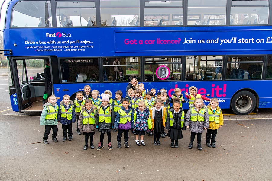 Photo of a group of school children wearing hi-vis jackets with the side of a bus visible behind.