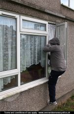 A man in a hooded top climbing in through an open window.