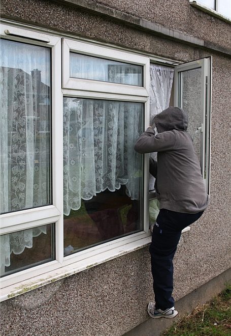 A man in a hooded top climbing in through an open window.