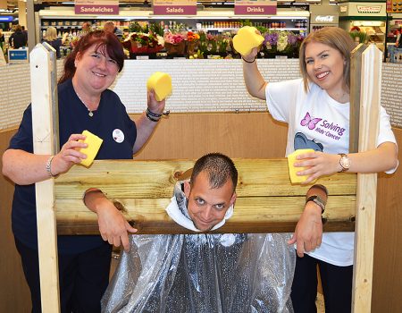Tesco Extra Bradley Stoke staff members Dawn Richards (community champion, left) and Katie Palmer (right) invite shoppers to throw wet sponges at Atilla Kiss (home delivery manager) to raise funds for the Kisses for Kaylum appeal.