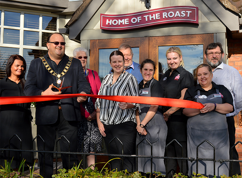 Photo of Cllr Andy Ward cutting the ribbon to reopen the Toby Carvery, watched by members of staff and volunteers from St Peter's Hospice.