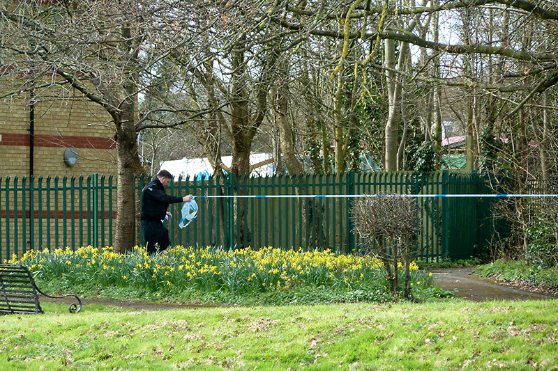 Photo of a police officer removing a tape barrier at the scene of the reported assault.