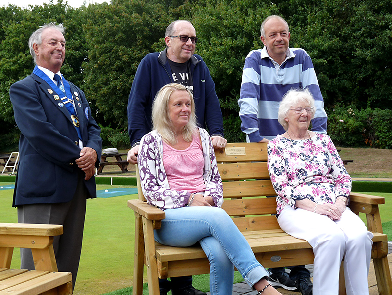 Photo of the bench dedicated to the memory of Jim Durlacher, with two people sitting on it and three people standing behind it.