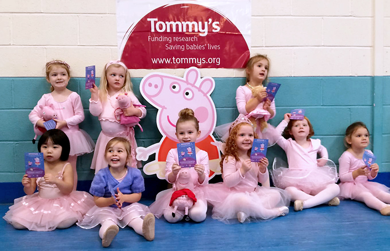 Photo of Babyballet Bradley Stoke pupils with the Tommy's charity logo on a wall behind them.