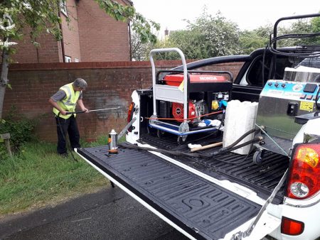 Photo of a BSTC operative using steam cleaning equipment to remove graffiti from a wall.