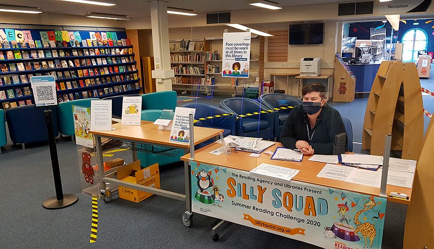 Photo of the inside of Bradley Stoke Library with a member of staff seated behind a screen and wearing a mask.