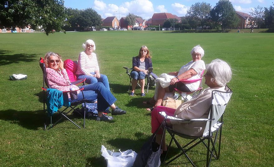 Photo of a group of ladies sitting on chairs in a field.