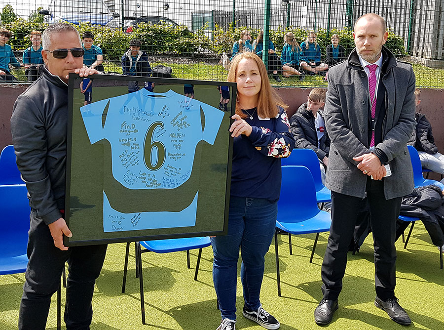 Photo of two people holding a framed football shirt.