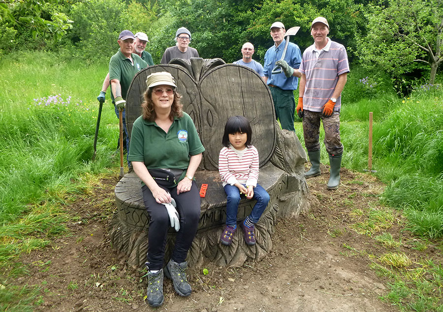 Photo of people standing around and sitting on a wooden sculpture.