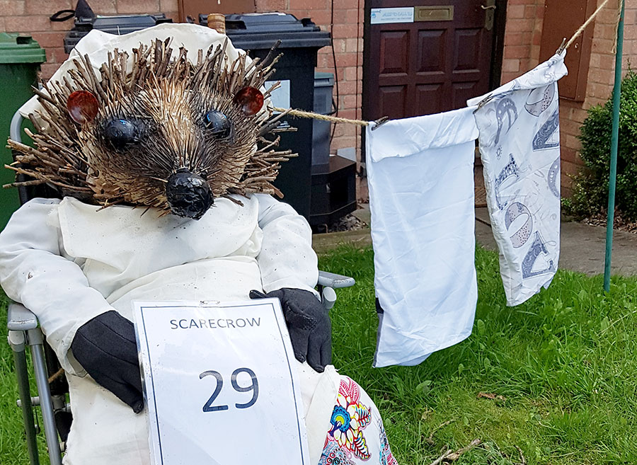Photo of a scarecrow in the form of a seated hedgehog wearing clothes.