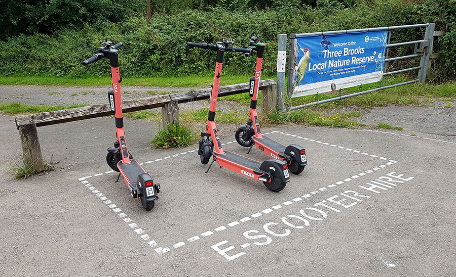 Photo of three e-scooters within a parking bay marked on the ground.
