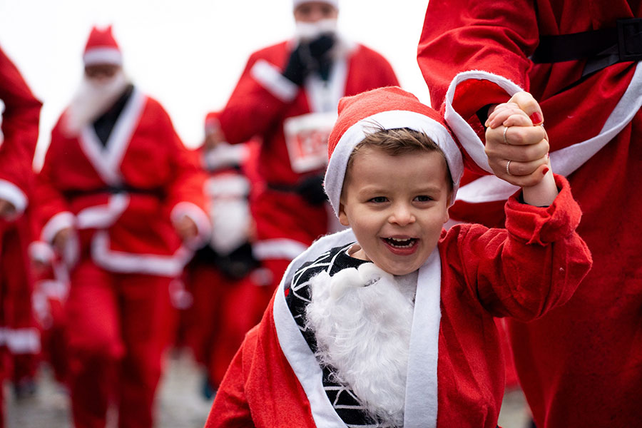 Photo of a child and adults dressed in Santa suits and running.