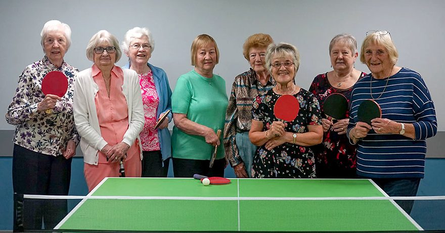 Photo of a group of ladies standing behind a table tennis table.