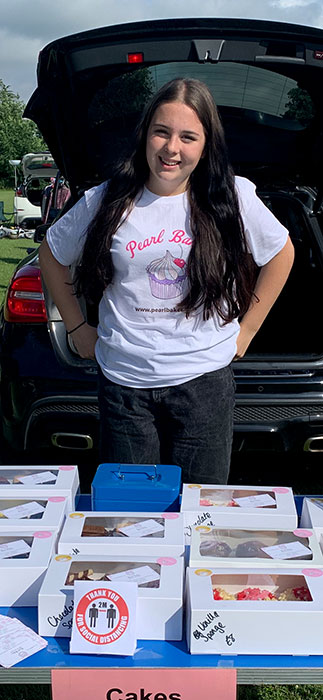 Photo of a person standing behind a table displaying cakes for sale.