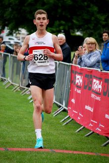 Adam Wilson crosses the line in first place. Photo of a runner.