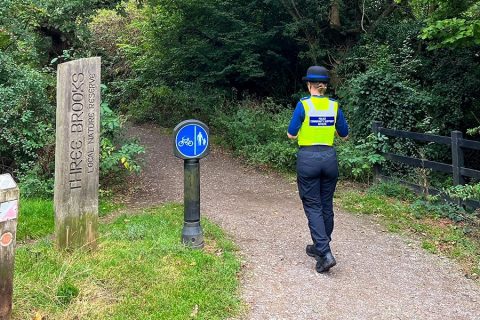 Photo of a police officer on patrol on a path through a woodland area.