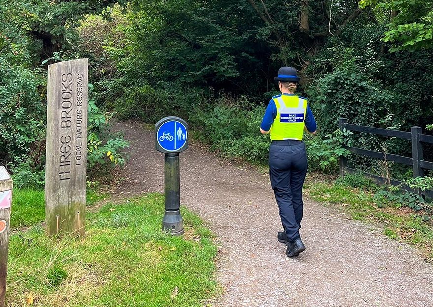 Photo of a police officer on patrol on a path through a woodland area.