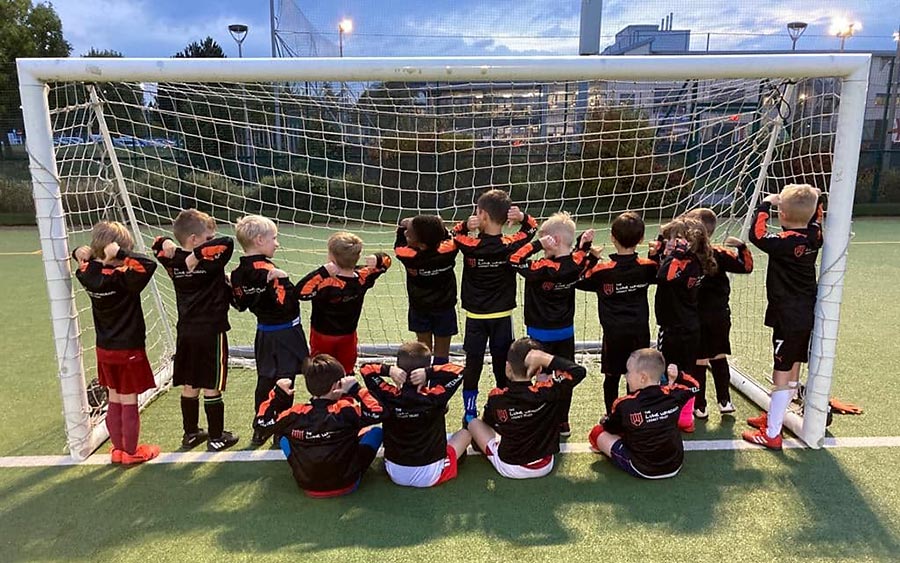 Photo of a youth football team standing in a goal mouth.