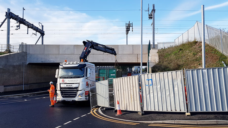 Photo of a lorry unloading a container close to a railway bridge.