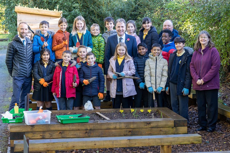 Photo of a large group of people standing in front of a raised bed in a garden.