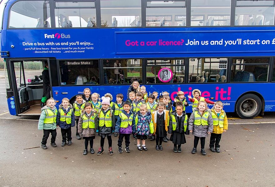 Photo of a group of school children wearing hi-vis jackets with the side of a bus visible behind.