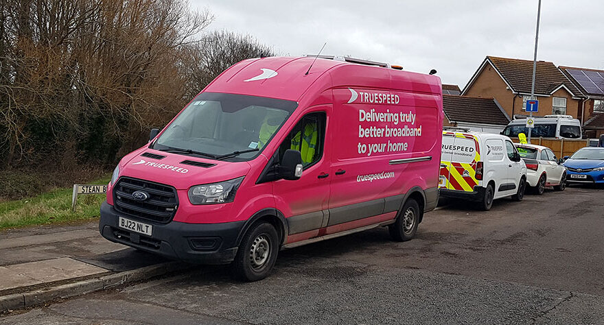 Photo of a pink van with Truespeed branding at the side of a road.