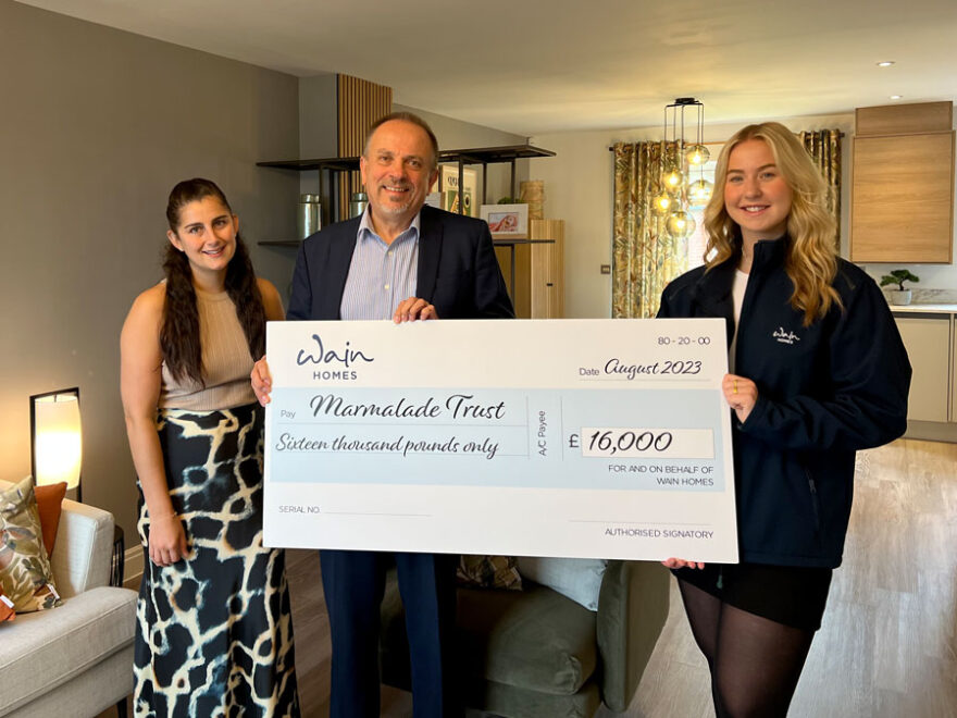 Photo of three people at a charity cheque presentation.