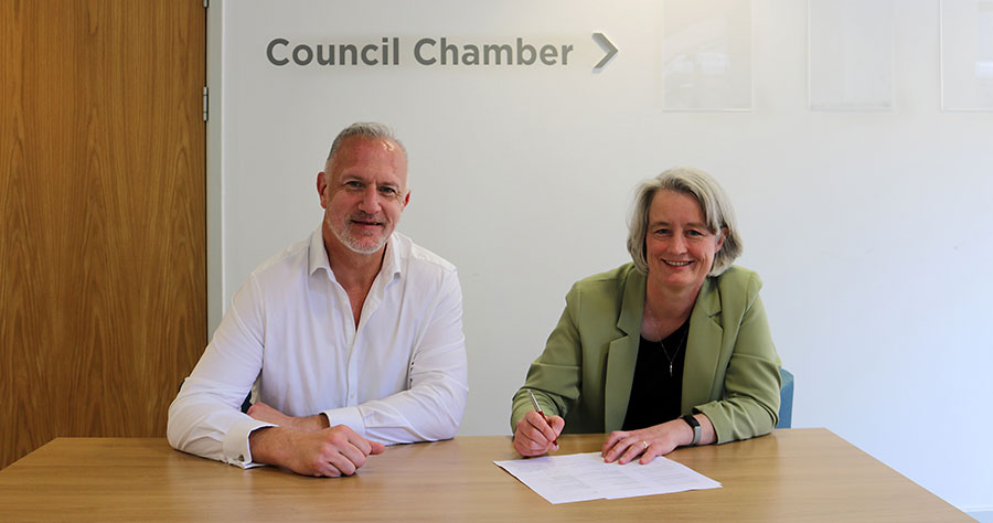 Photo of two people seated at a table and signing an agreement.
